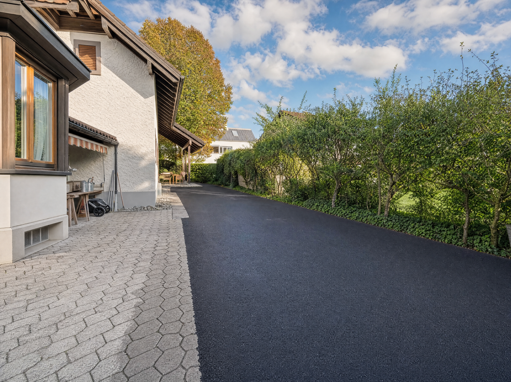 Sanierte Hofeinfahrt mit alter Pflastersteinverbund links und neuem Asphalt rechts, klare Architektur
